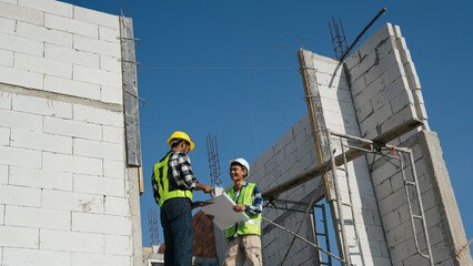 Structural engineer and architect working with blueprints discuss at the outdoors construction site.