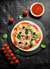 Raw pizza with cherry tomatoes, cheese, olives and spinach.