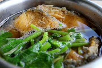 Fried fish(piece) and chinese celery, young ginger slice in broth, Chines style soup in stainless bowl.