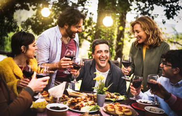 Young men and women having fun drinking out at wine diner - Food and beverage life style concept on mixed age people enjoying time together at villa patio - Warm filter with bulb string lights halo - 562169247