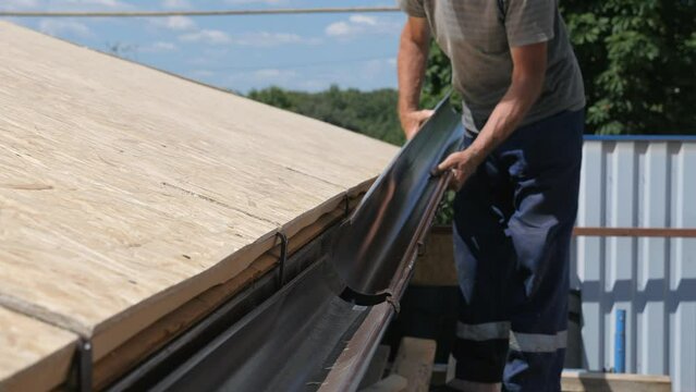 Installation of a drainage system. Drainage chute on a private house. The master roofer connects the drain pipes. Work at height, danger. Summer, heat. Construction of a private house. High-altitude