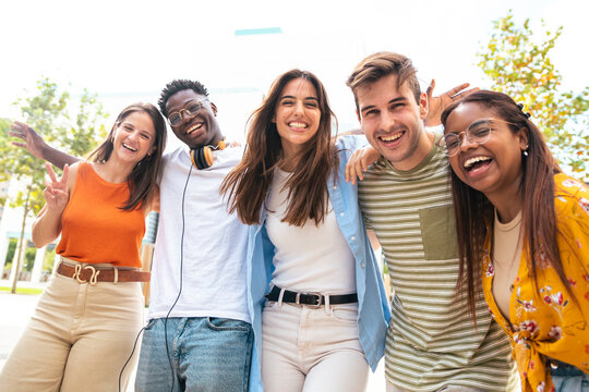 Low angle view of a happy group of multiracial friends looking at camera, enjoying outdoors. Multiethnic cheerful young people