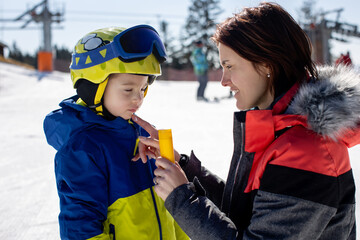 Mother, applying sun cream on her skiing child, family on ski winter vacation, skiing, taking measurment against the harsh sun