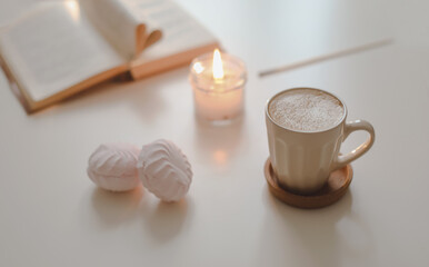 coffee cup, flower, candle and a book on a white table background top view