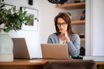 Attractive middle aged business woman sitting at home and using laptop for work