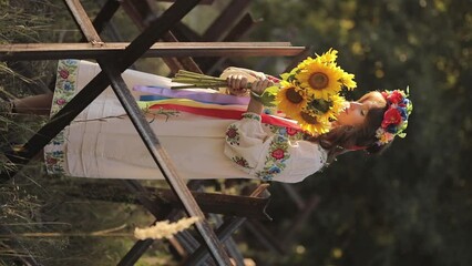 A beautiful Ukrainian girl in a Ukrainian national vyshyvanka dress with a bouquet of sunflowers against the background of anti-tank hedgehogs. war in Ukraine. War of Russia against Ukraine. - Powered by Adobe