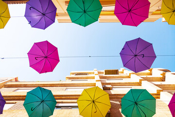 Street with bright, multi-colored umbrellas against the sky with houses.