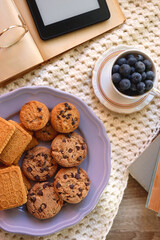 Plate of cookies, cup of tea, fresh blueberries, dry oranges, stack of books, reading glasses and tablet on the table. Hygge at home. Flat lay.