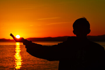 silhouette of a boy in the sunset holding the sun