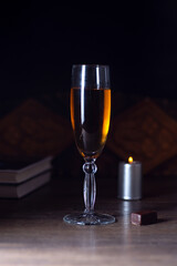 On the table is a glass of wine. A candle burns behind. Low key.