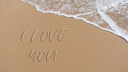 phrase I love you written in the sand of the beach