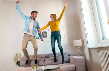 Young couple spending time together at home. Man and woman jumping on the couch and having fun
