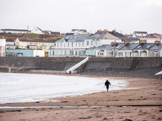 People walking on Kilkee beach and town houses in the background. County Clare, Ireland. Nobody. Popular summer resort. Atlantic ocean, Irish seascape. Cloudy sky.