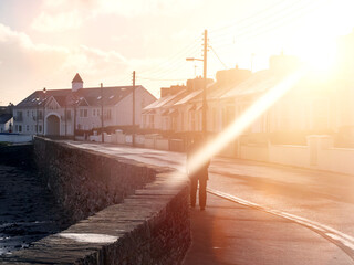 Person walking on a foot path in a street at sunrise. Warm color and sun flare. Small town...