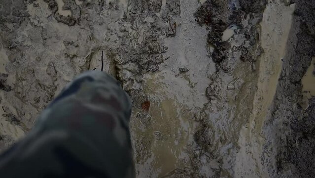 Close-up of the legs of a man walking in military camouflage with trekking rubber boots dirty in the mud