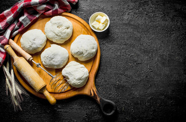 Round pieces of dough on a cutting Board with a rolling pin and a whisk.