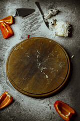 empty board after pizza on a black background; on a black background there is an empty board with pizza, scattered flour, pepper, mushrooms and utensils