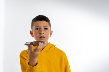 handsome little boy is happy with the phone in hand, dressed in yellow hoodie, isolated on grey background, copy space