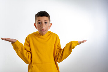 cute boy kid wearing casual yellow hoodie clueless and confused expression with arms and hands raised. doubt concept.