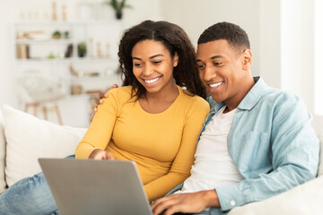 New normal and chat at home. Cheerful young african american couple watch video on laptop, have...