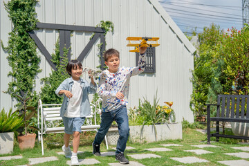 Two boys look fun with hold plane model and run in home garden with warm light in concept of outdoor activity to get better health and creative talent.
