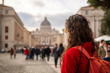 Woman in red coat looking at St. Peter's Basilica in Rome from the bridge that leads straight up to...