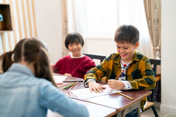 Little Asian boy look happy with smiling and look to his friend draw and paint the picture in class...