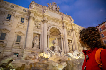 Woman looks at the Trebi Fountain in the middle of Rome, one of the largest fountains in the city, seen at night