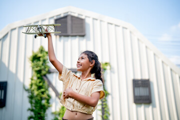 Asian girl enjoy to play with plane model in home garden or yard with warm light and blue sky in...