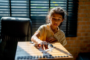 Little Asian girl concentrate and practice to play board game call Go in her father working room...