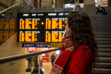 Woman with red coat in Europe train station watching timetables on screen