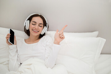 Tranquill brunette lady listening to music in bed, using smartphone