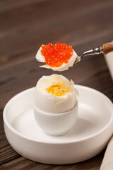 Boiled egg partially peeled from the shell in a stand, red caviar on top