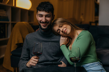 Front view of a beautiful affectionate young couple spending evening together with some red wine