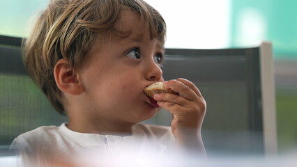 Little toddler eating bread at table. child boy eats carb food