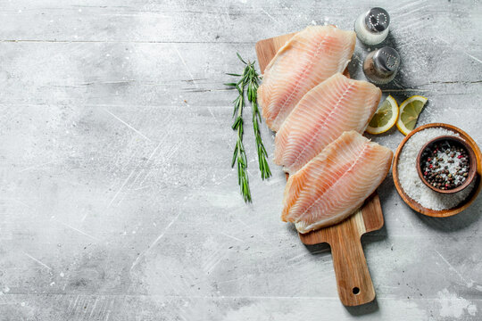 Fish fillet on a wooden cutting Board with rosemary, spices and lemon slices.