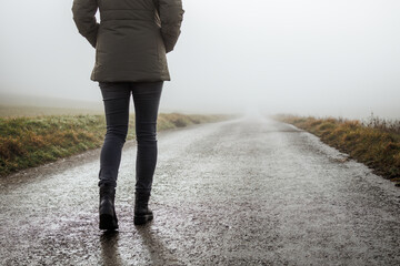Person in fog walking to nowhere. Lonely woman on empty road alone. Concept of uncertain future