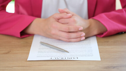 Female manager is sitting at her office desk with contract paper and pen close-up.