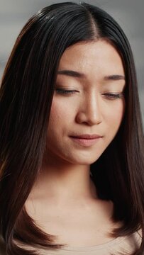 Vertical video: Female model embracing imperfections for self love ad, asian girl feeling flawless and posing to promote nourishing skincare products. Beautiful woman with natural bare skin in studio.