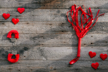 BDSM accessories on a wooden background. Red soft fluffy handcuffs and a leather whip lie next to each other. Sex accessories gift for valentine's day