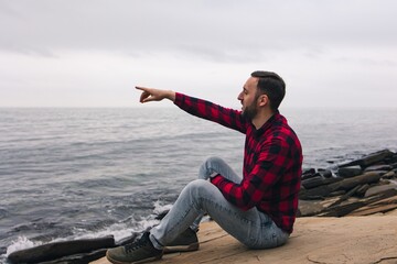
Side view of a tourist pointing with his hand in the right direction.
Man traveler explores the area. Healthy lifestyle and outdoor activities near the sea.