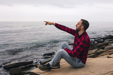 
Side view of a tourist pointing with his hand in the right direction.
Man traveler explores the area. Healthy lifestyle and outdoor activities near the sea.