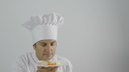 the chef smells the plate, white cap and uniform, smiling face