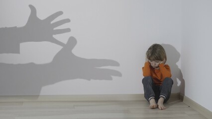 Shadows of parent hands aggressive gestures over squatting child in the corner