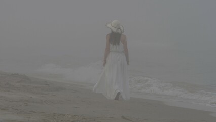 Isolated woman with back walk on foggy, misty beach, stormy wave, lonely feeling