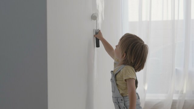 Portrait of amusing little child painting white walls, serious boy