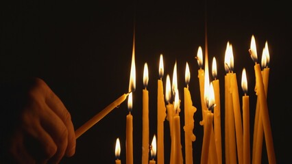 Detail of hand taking holding a candle take light from other candle, sharing