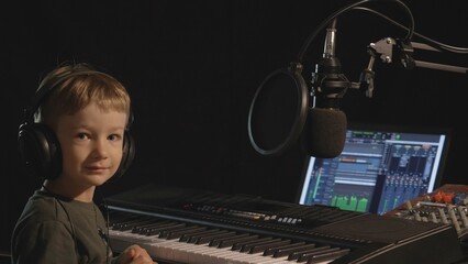 Funny little child with headphones play at piano, little music producer