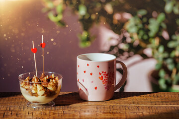 tiramisu cake and a mug of tea with drawn hearts stand on a wooden background, valentine's day celebration, declaration of love. blur light effect on background