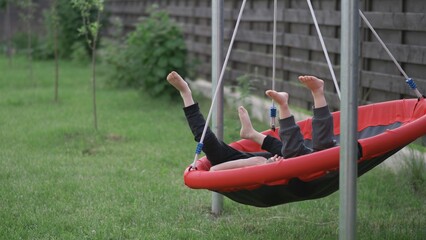 Two kids playing barefoot in the yard spinning nest swing - obrazy, fototapety, plakaty